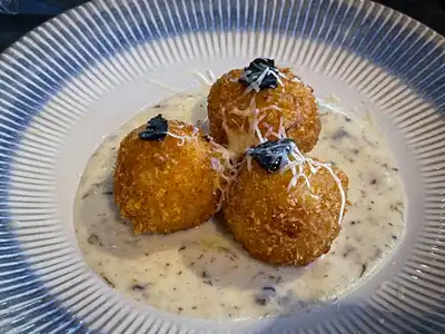 Three fried rice balls on a cream sauce, topped with grated cheese, on a ridged plate