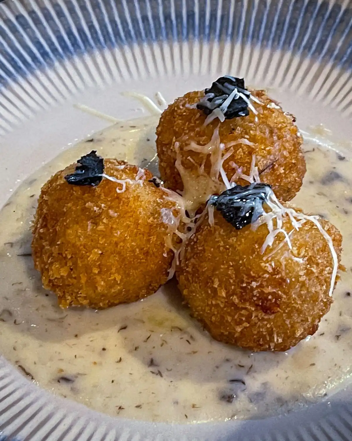 Three fried rice balls on a cream sauce, topped with grated cheese, on a ridged plate