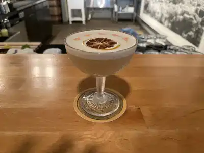 A frothy sour in a stemmed glass with a dried citrus wheel, on a wooden bar