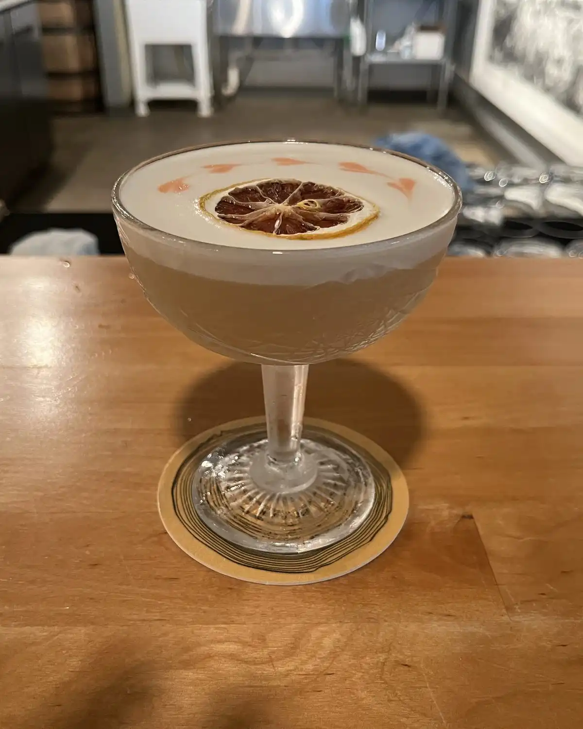 A frothy sour in a stemmed glass with a dried citrus wheel, on a wooden bar