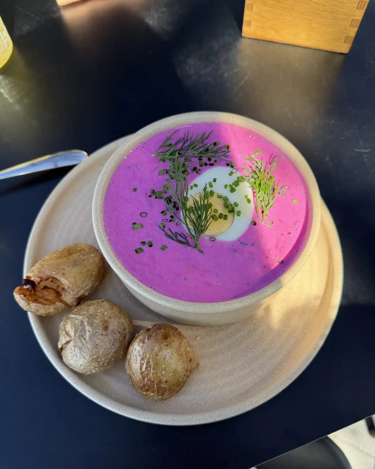 A bowl of cold pink beet soup with dill and half an egg, with small rolls on the side