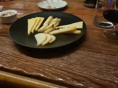 Slices of hard cheese on a black plate beside a glass of red wine on a wooden bar