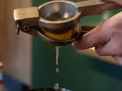 A bartender squeezing a lemon through a hand press into a cocktail shaker