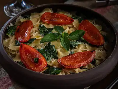 Farfalle with roasted tomato halves, spinach and basil in a dark bowl