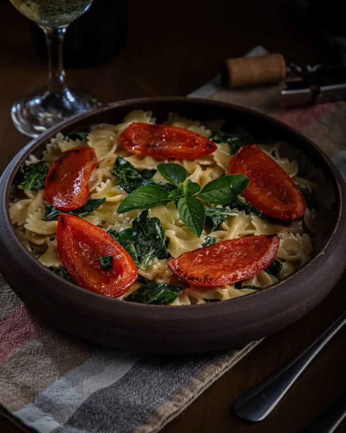 Farfalle with roasted tomato halves, spinach and basil in a dark bowl