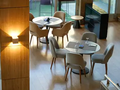 Round tables with grey chairs beside a wall lamp on a wooden pillar