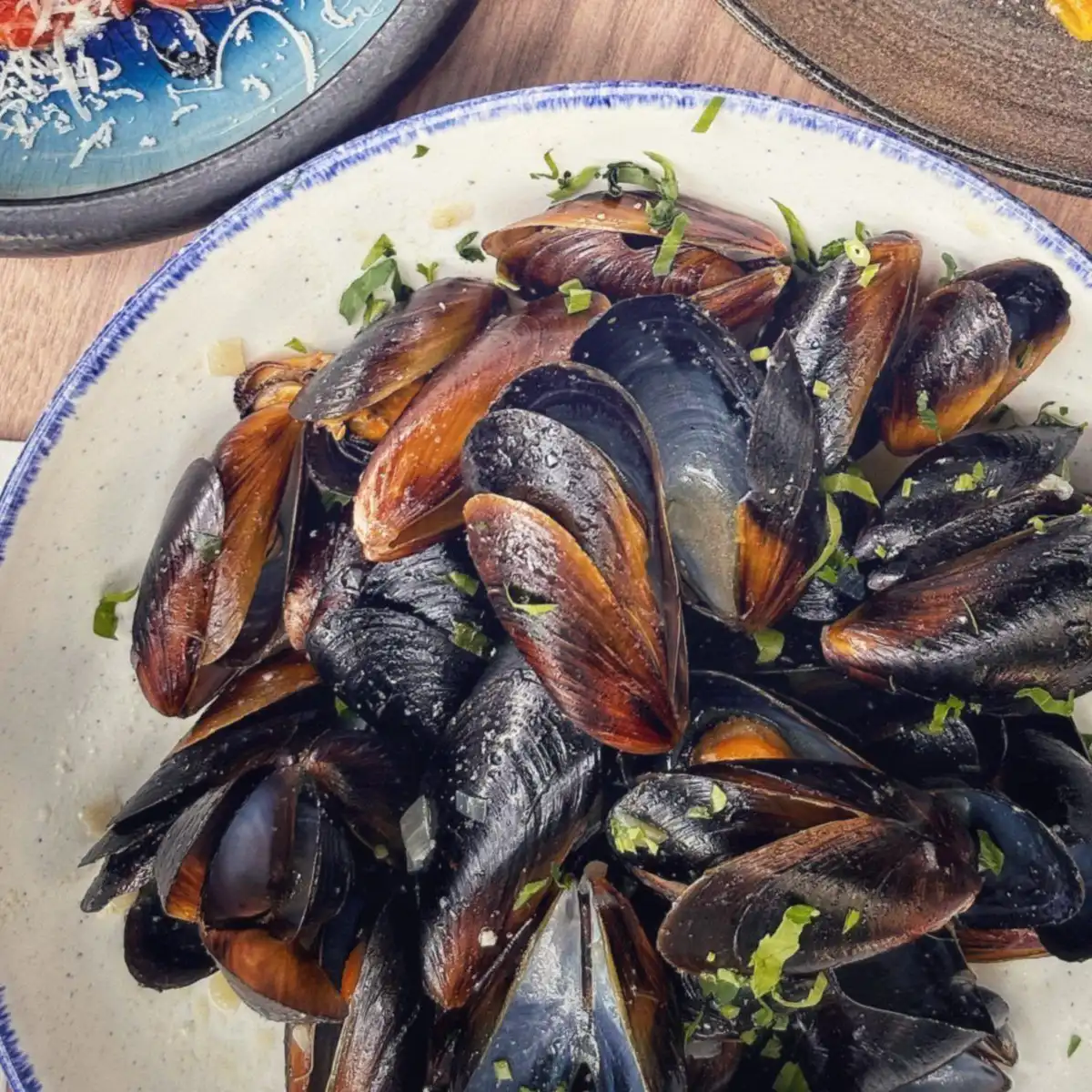 A white bowl of steamed mussels scattered with parsley