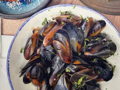 A white bowl of steamed mussels scattered with parsley