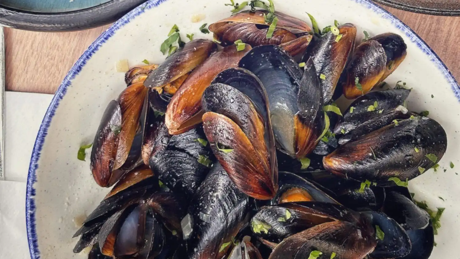 A white bowl of steamed mussels scattered with parsley