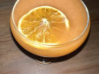 An orange cocktail in a coupe with a dried orange slice floating on top