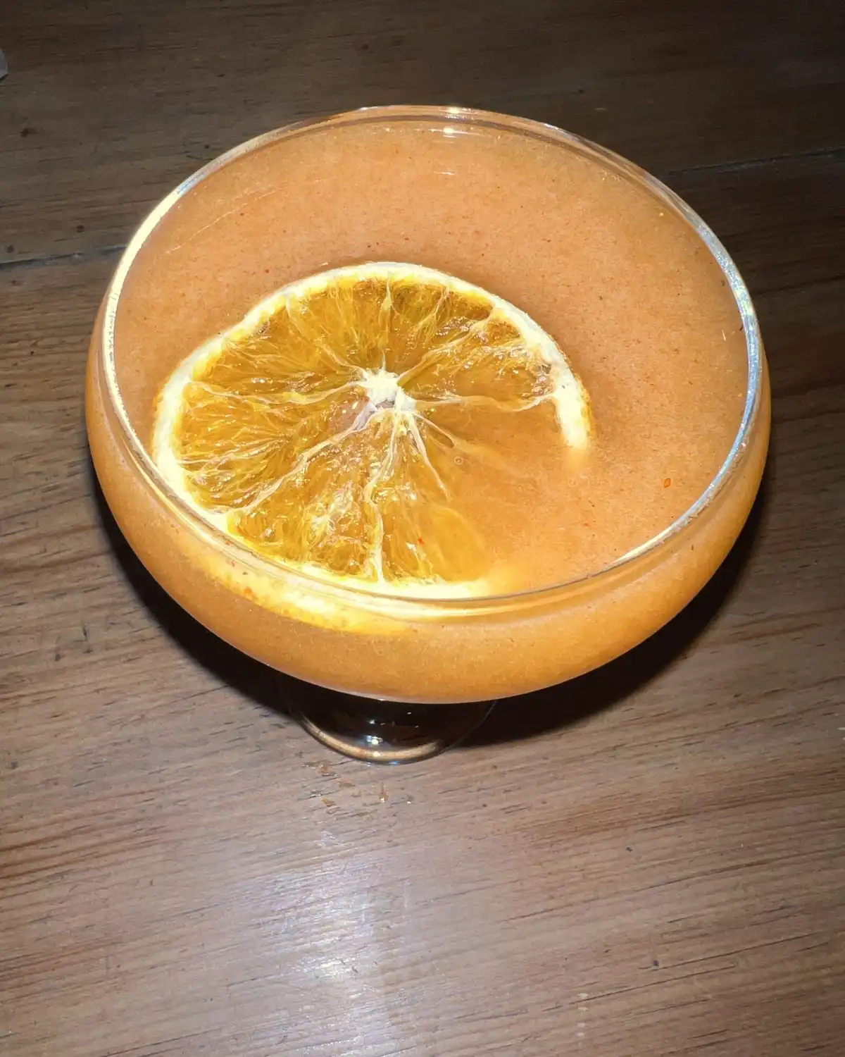 An orange cocktail in a coupe with a dried orange slice floating on top