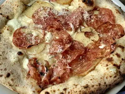 A pizza with salami, thin potato slices, rosemary and grated parmesan