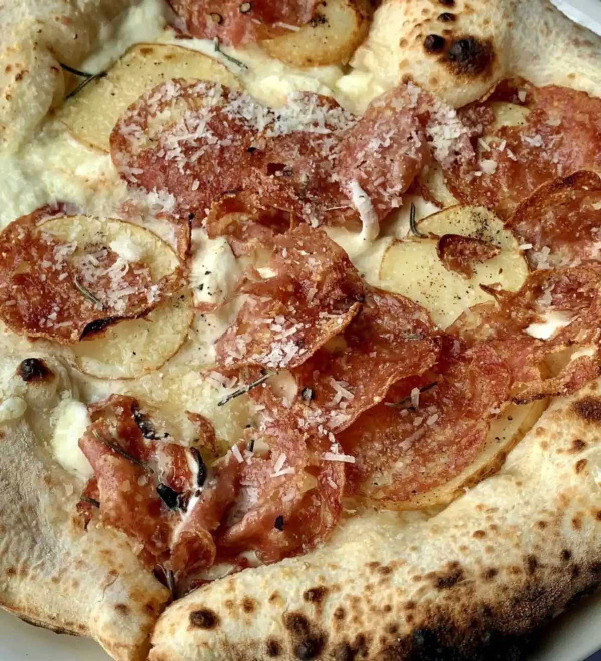 A pizza with salami, thin potato slices, rosemary and grated parmesan