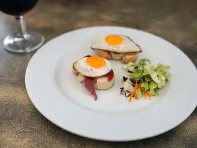 Small toasts topped with cured ham and fried quail eggs, with a side salad, on a white plate