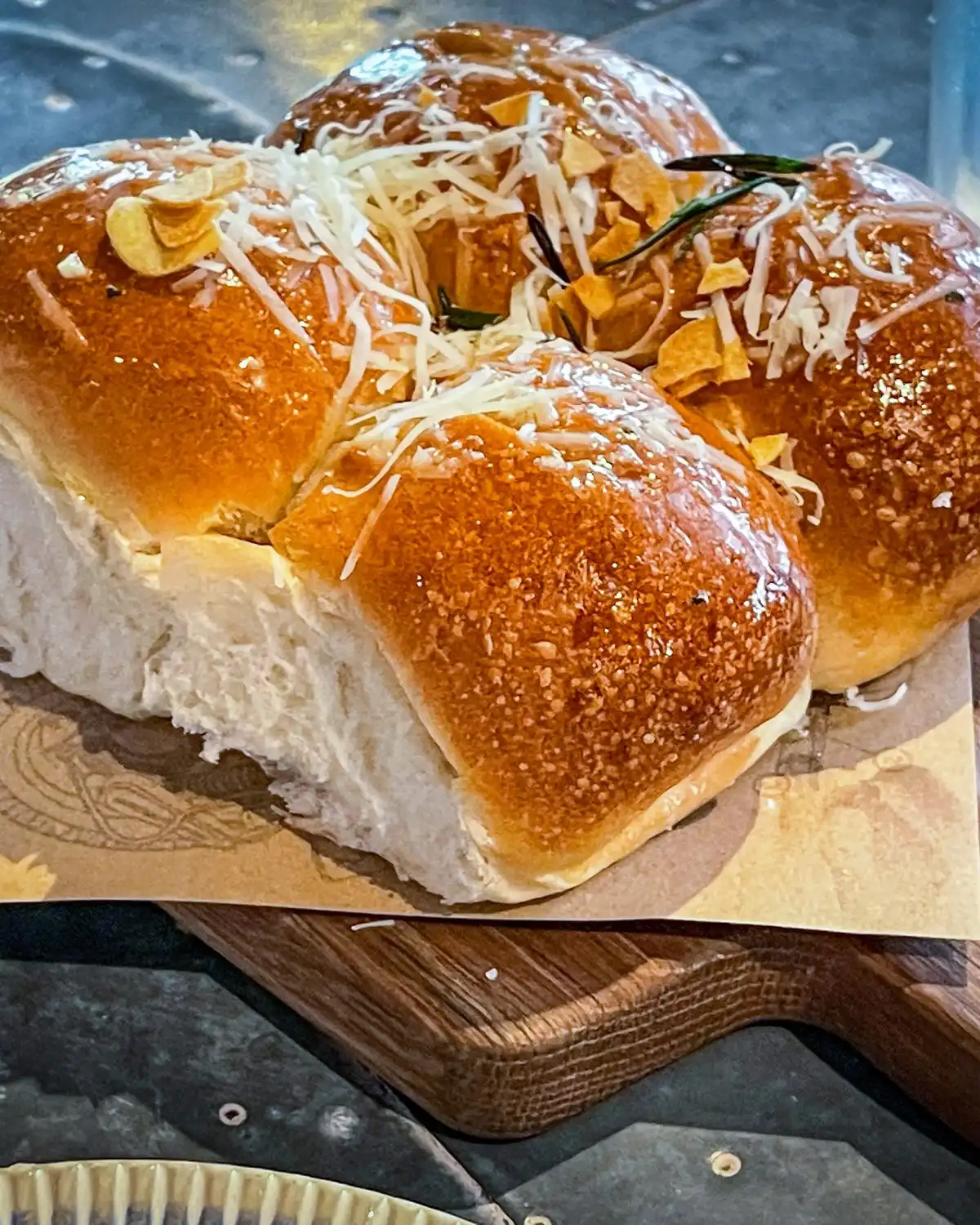 Glazed milk buns topped with grated cheese on a wooden board