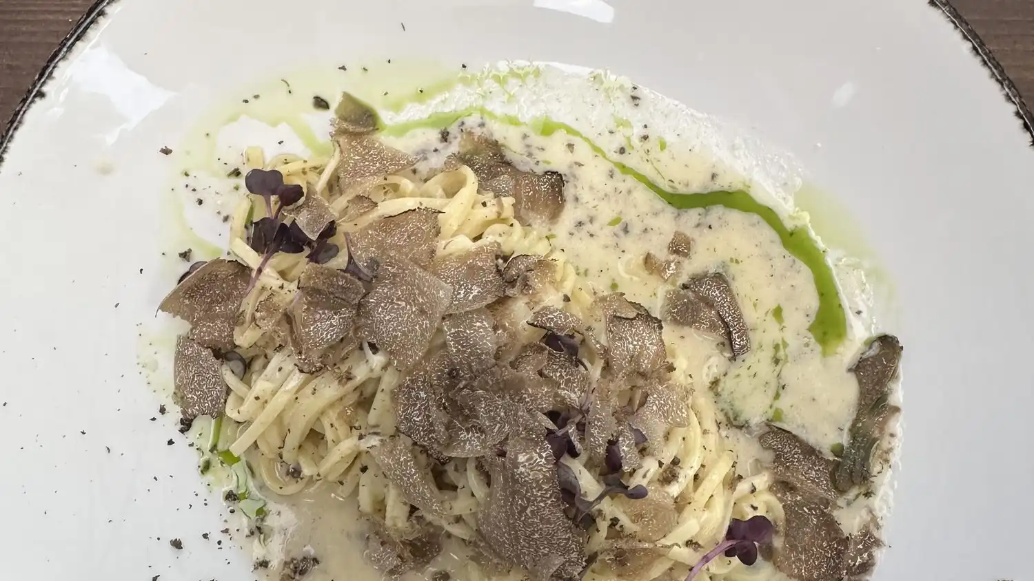 Tagliolini in a cream sauce with shaved black truffle and a line of green oil on a white plate