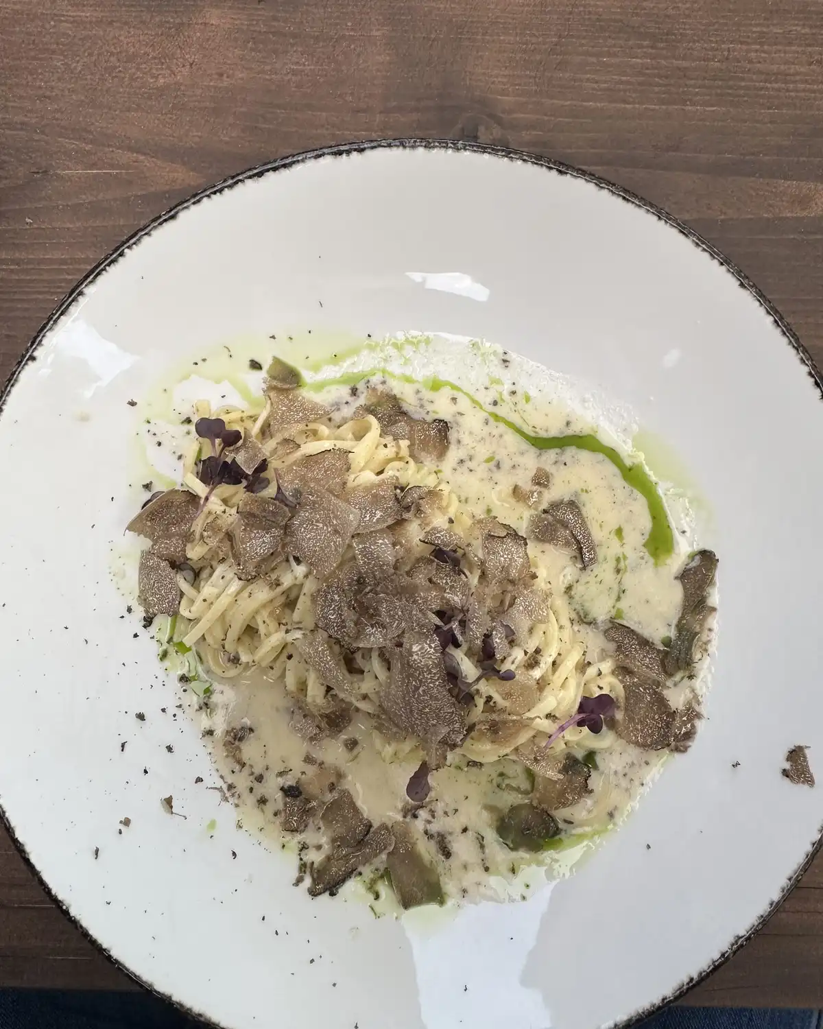 Tagliolini in a cream sauce with shaved black truffle and a line of green oil on a white plate