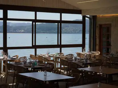 A dining room of set tables in front of long windows over the water