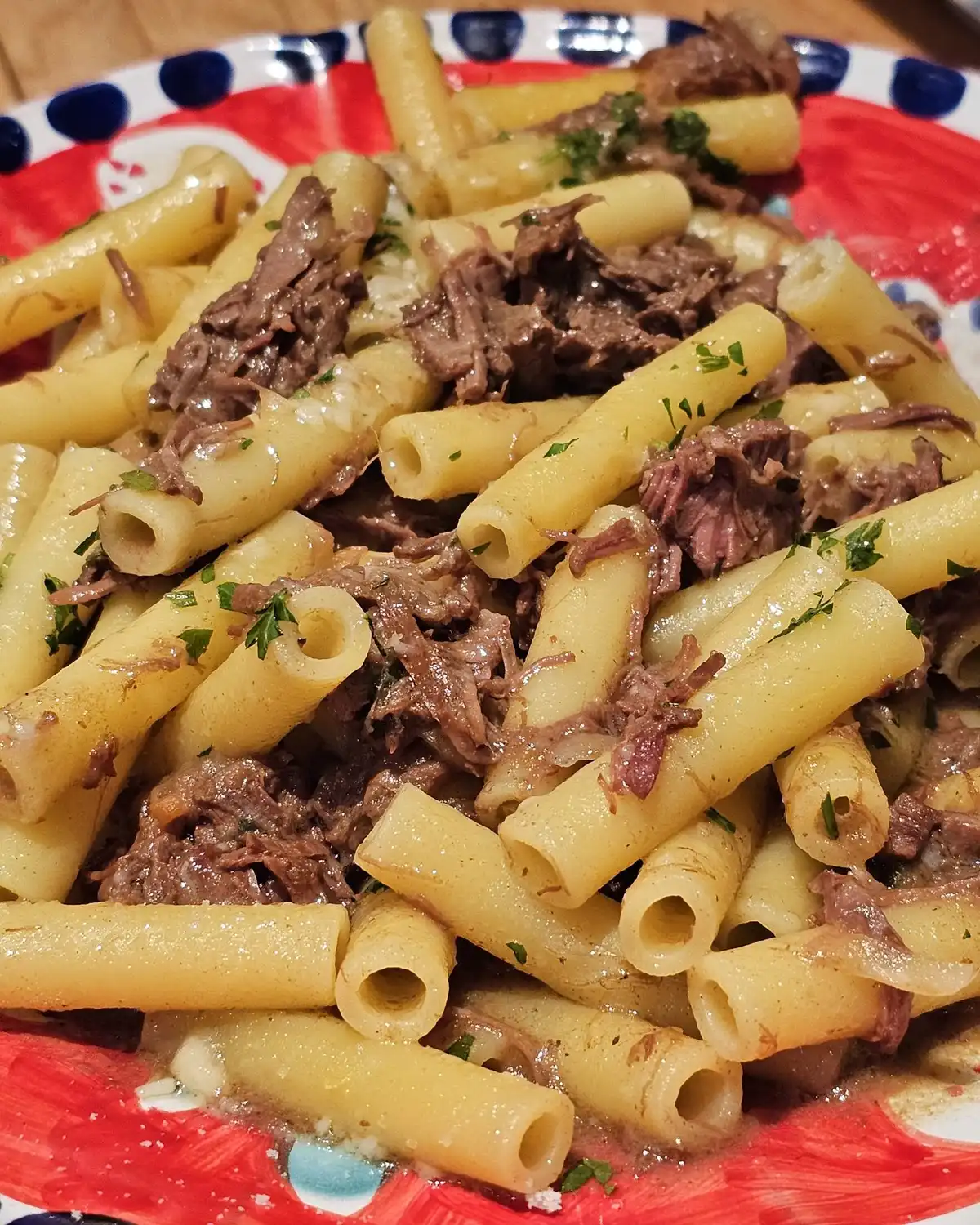 Ziti tossed with slow-cooked beef and onion on a red and blue painted plate