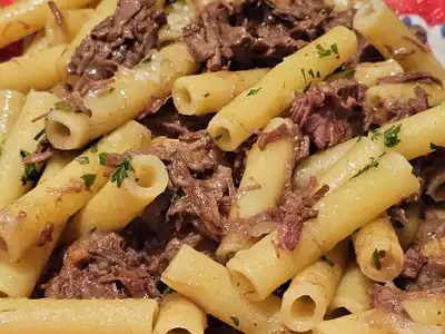 Ziti tossed with slow-cooked beef and onion on a red and blue painted plate
